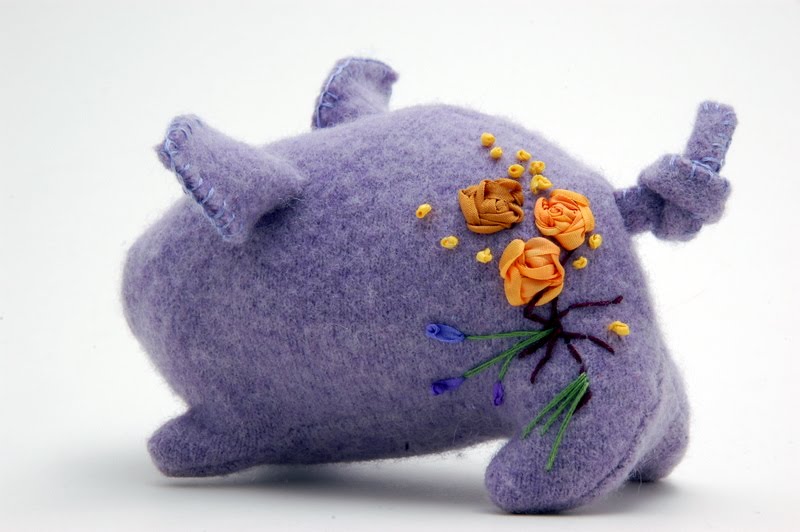 a small purple pig with embroidery on his bottom faces away from the camera.