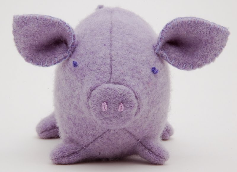 A small purple woolen pig. He has large ears and pink embroidered nostrils.