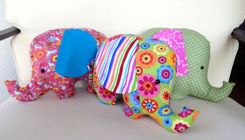 Three stuffed elephants in psychadelic colors sit on a sofa