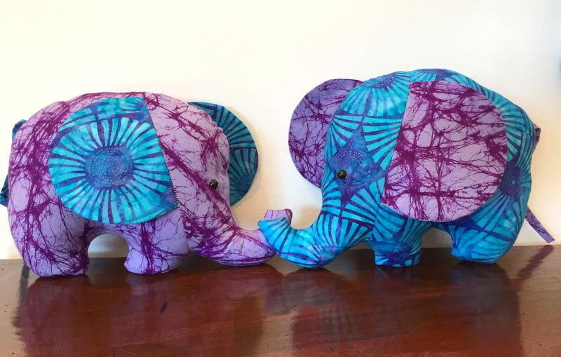 Two stuffed elephants face each other - they are sewn from blue and purple batik fabric.