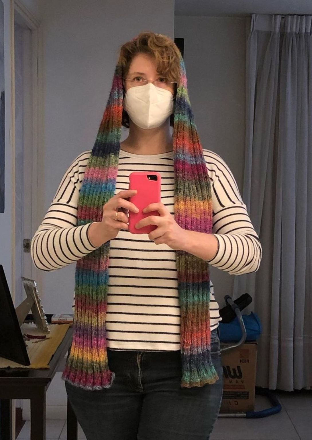 A woman drapes a rainbow striped wool scarf over her head