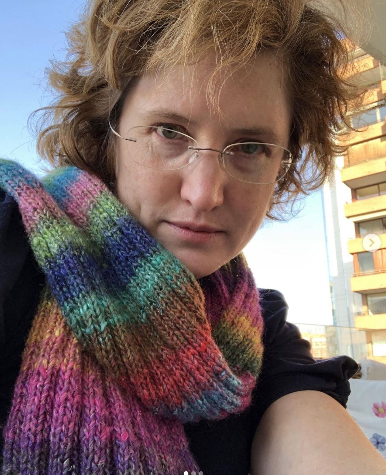 A woman looks down at the camera wearing a striped wool scarf
