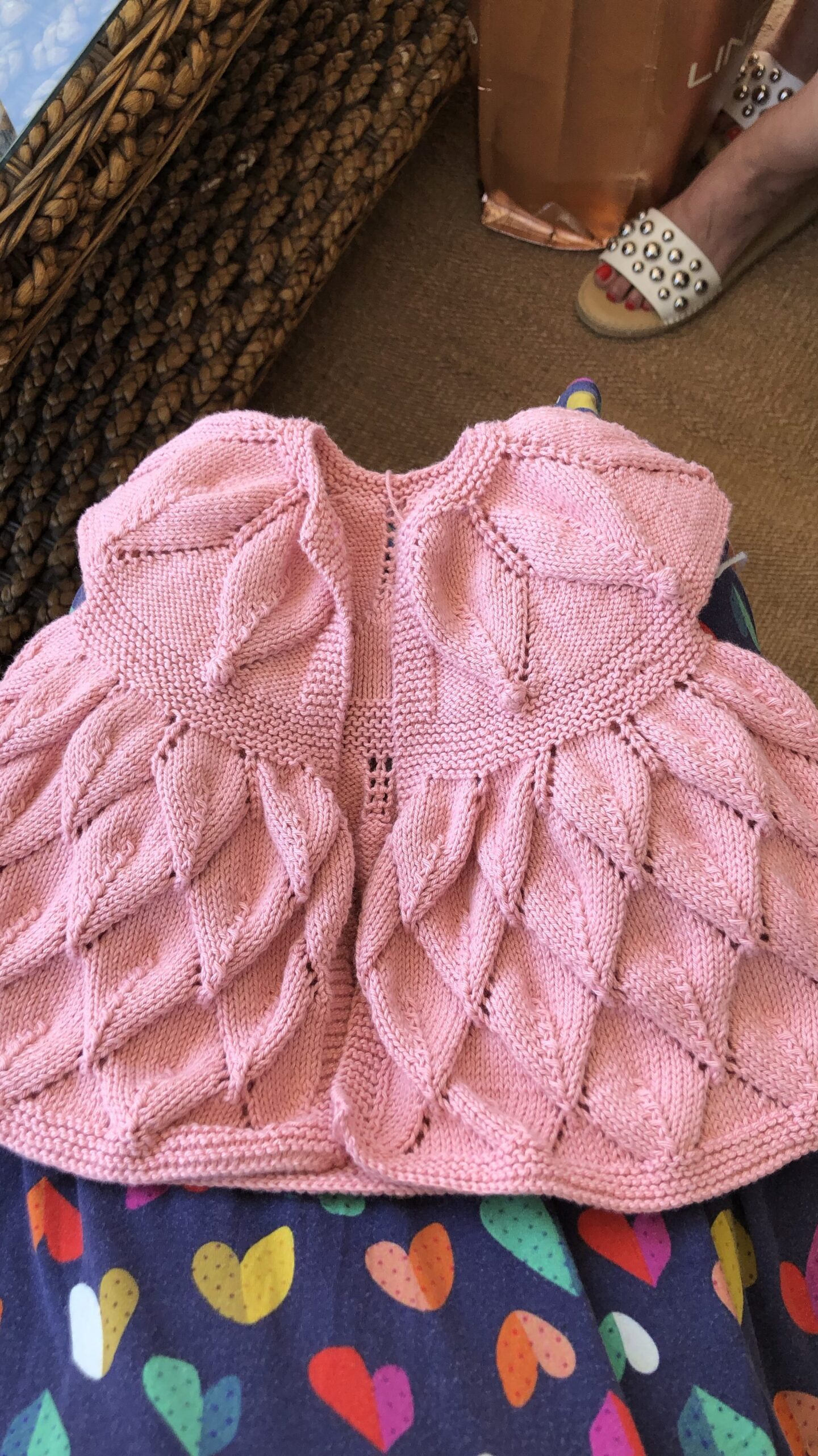 A pink knitted baby dress with complicated stitching that looks like leaves