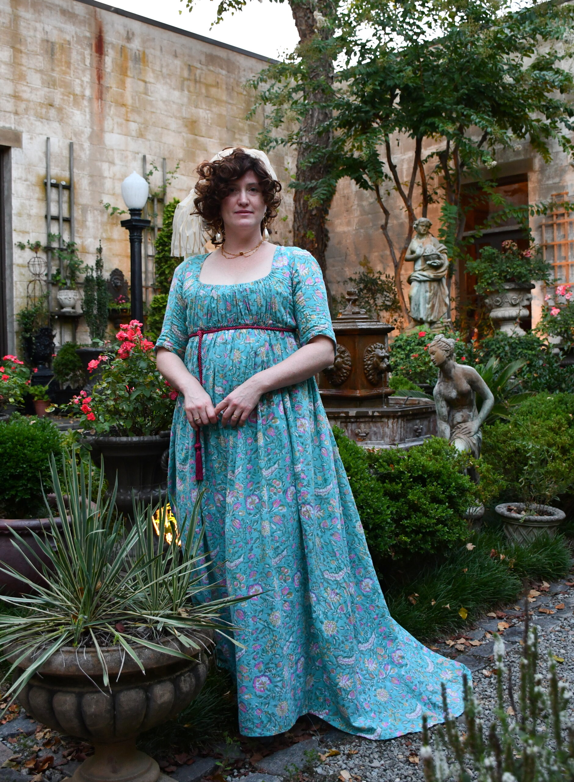 Tabubilgirl stands in a garden wearing a floral cotton 1790s round gown