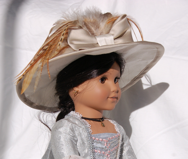 An American Girl doll wears an enormous edwardian hat decorated with feathers and a bow