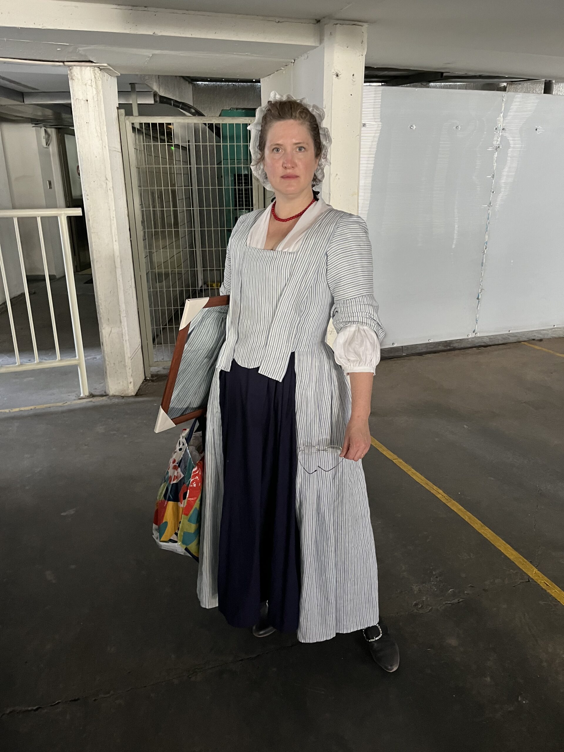 Tabubilgirl stands in a modern parking garage wearing a 1750s linen english nightgown. she looks hot and wilted.