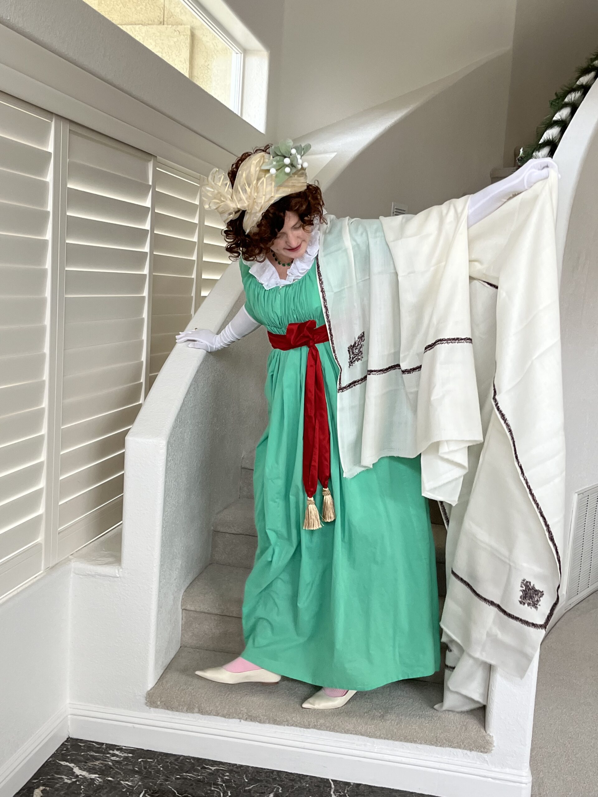 Tabubilgirl stands on a stair wearing a green 1790s round gown. A large cream shawl is draped over her arm