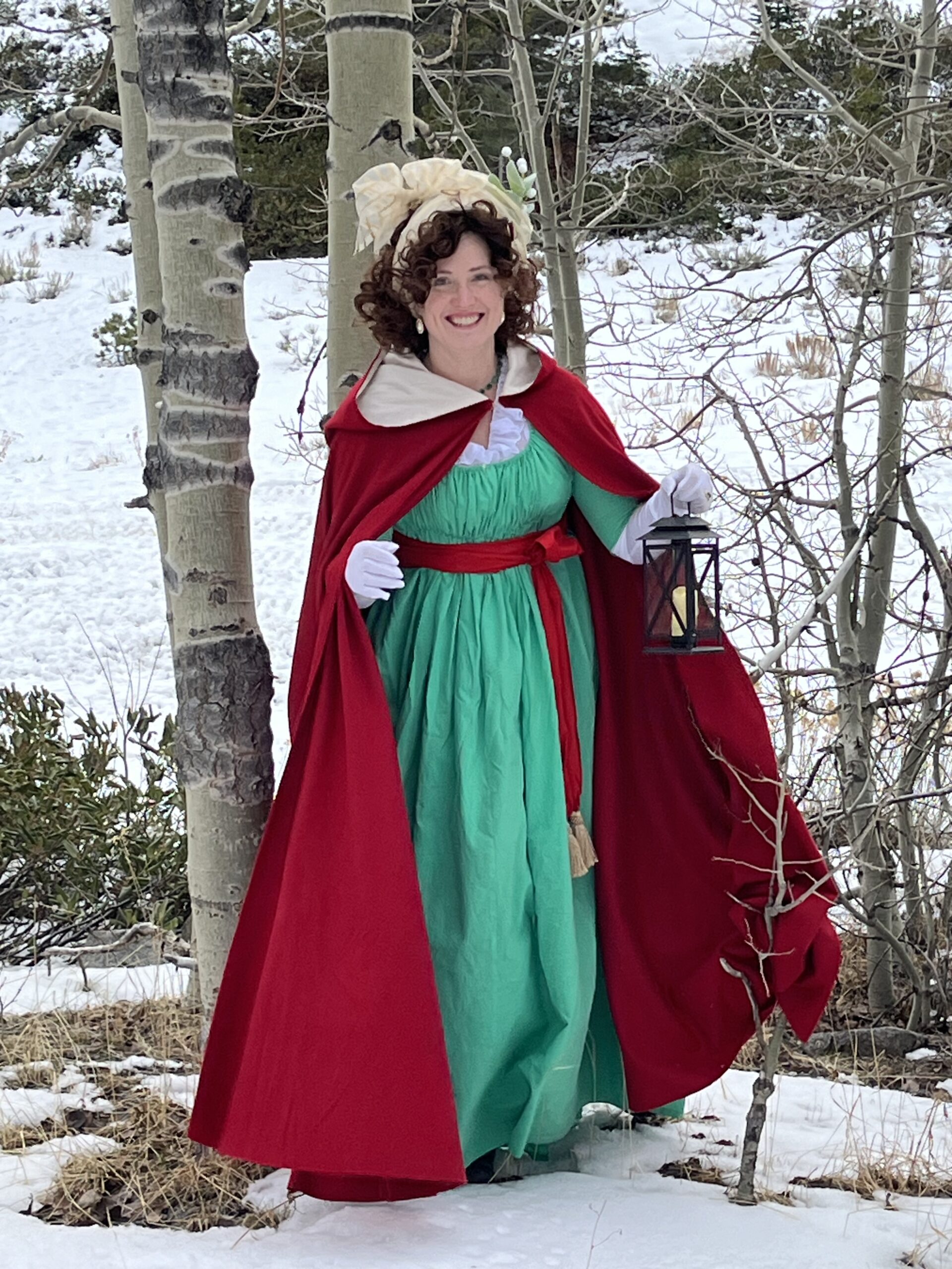 Tabubilgirl wears a 1790s New Year ensemble - a green 1790s New Year gown and red cardinal cloak. She carries a lantern