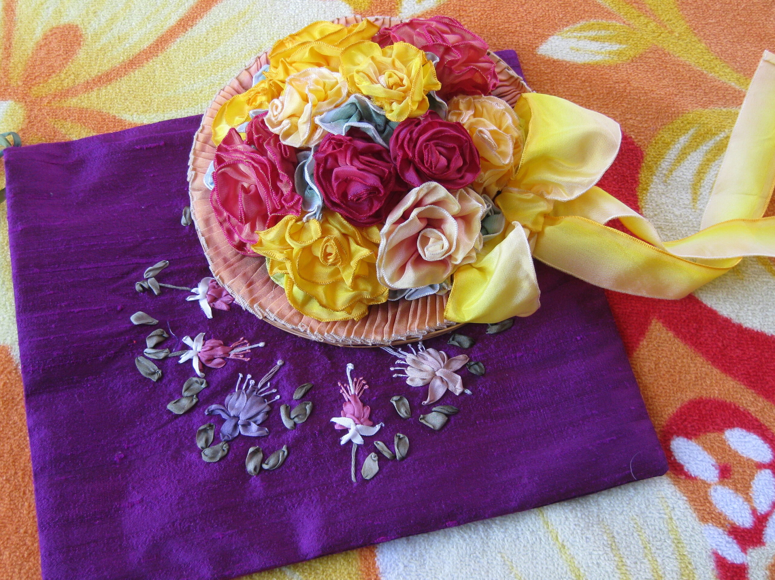 A doll hat covered in wired ribbon roses rests on a purple silk pouch embroidered with silk ribbon flowers