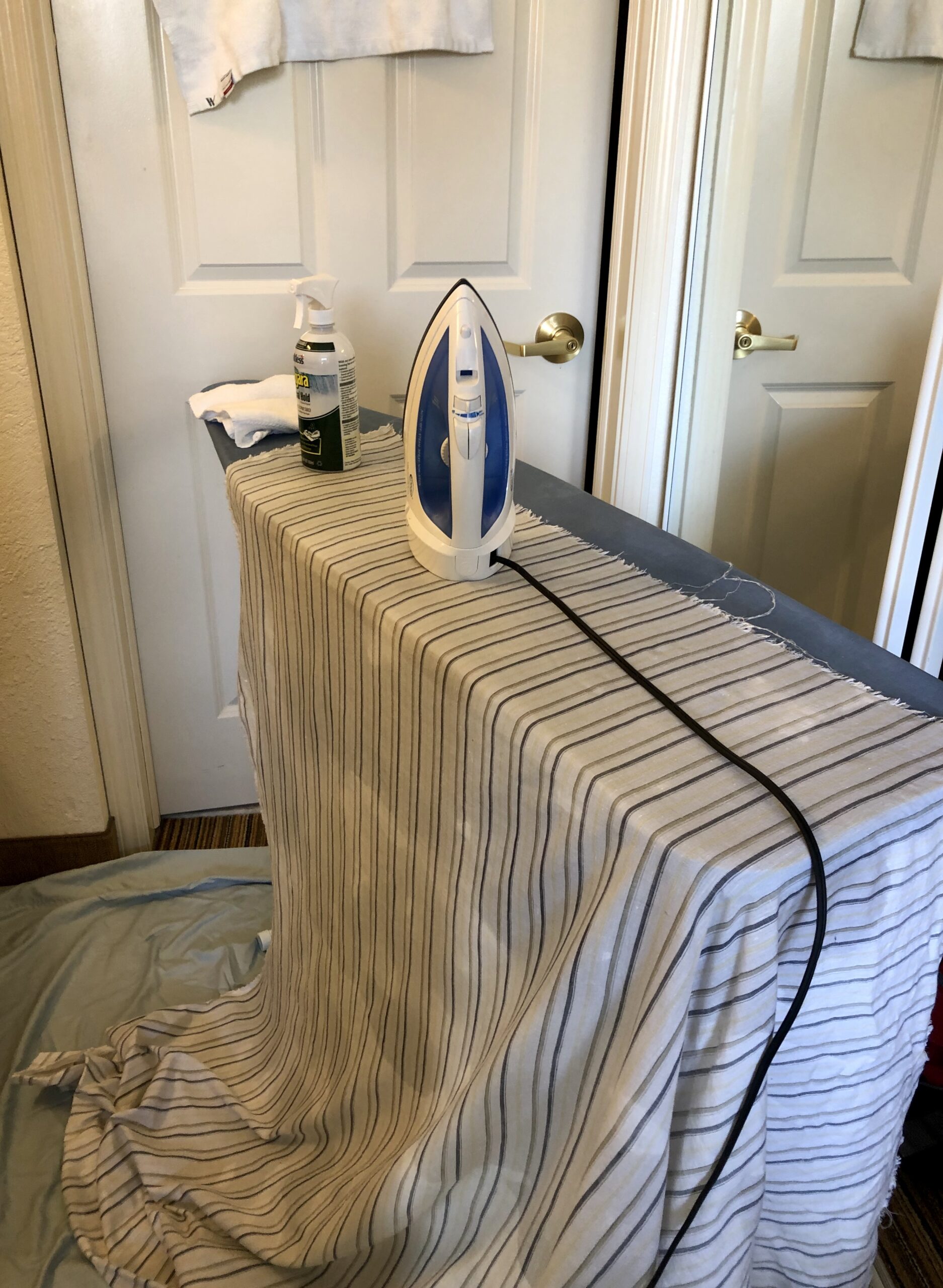 A blue ironing board is draped with a large piece of striped fabric - pale blue and yellow on white.  An iron sits on top of the fabric.  It is a very businesslike image.