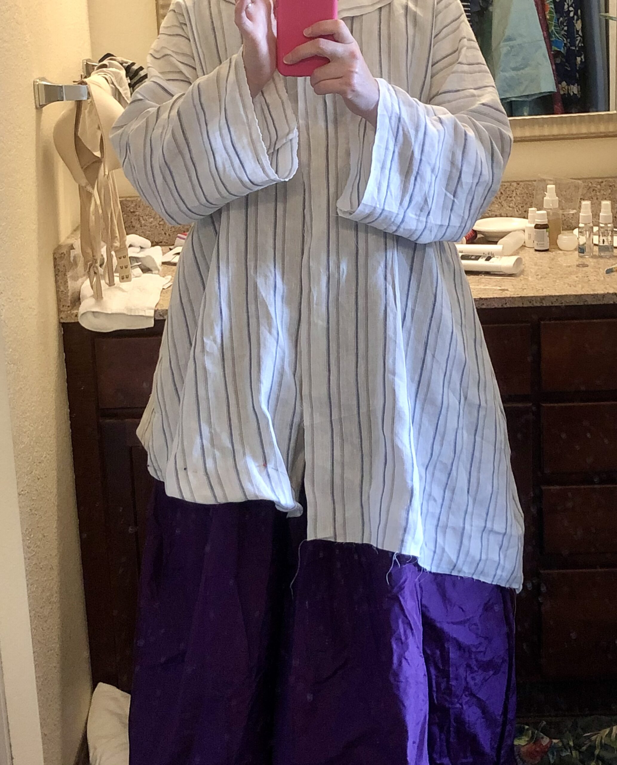 A woman is testing the fit of the Burnley and Trowbridge 18th century bedgown pattern. She is wearing the linen bedgown over an eggplant purple silk petticoat