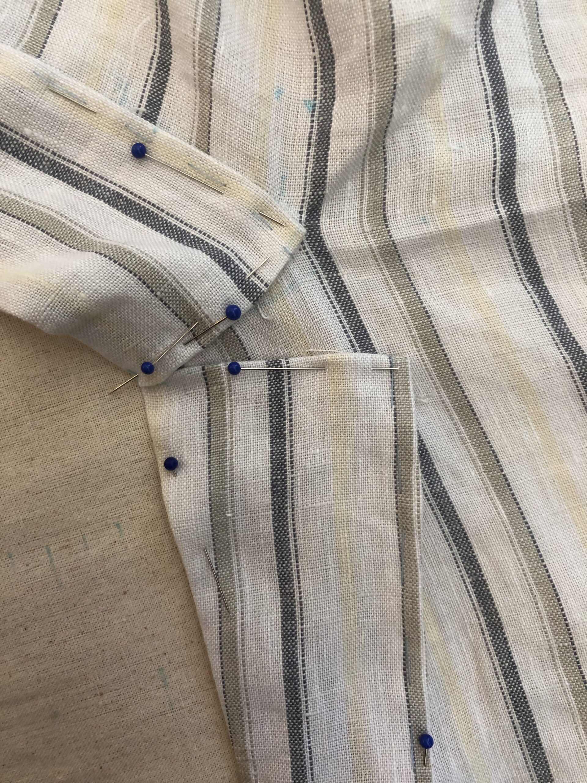 A close up of pins holding the seam allowances of the split collar on an 18th century linen bedgown