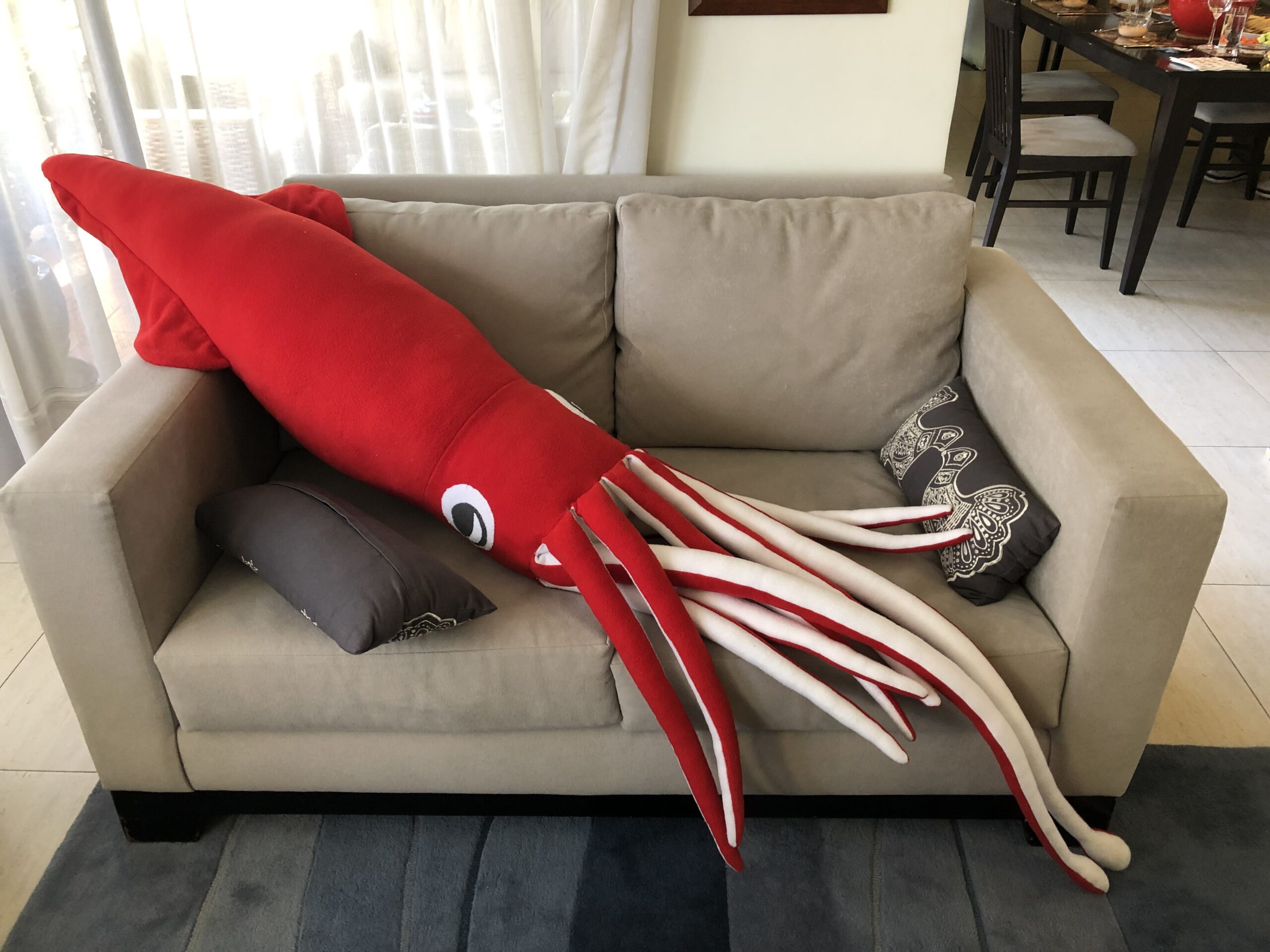 A giant red christmas squid sprawls across a grey sofa.