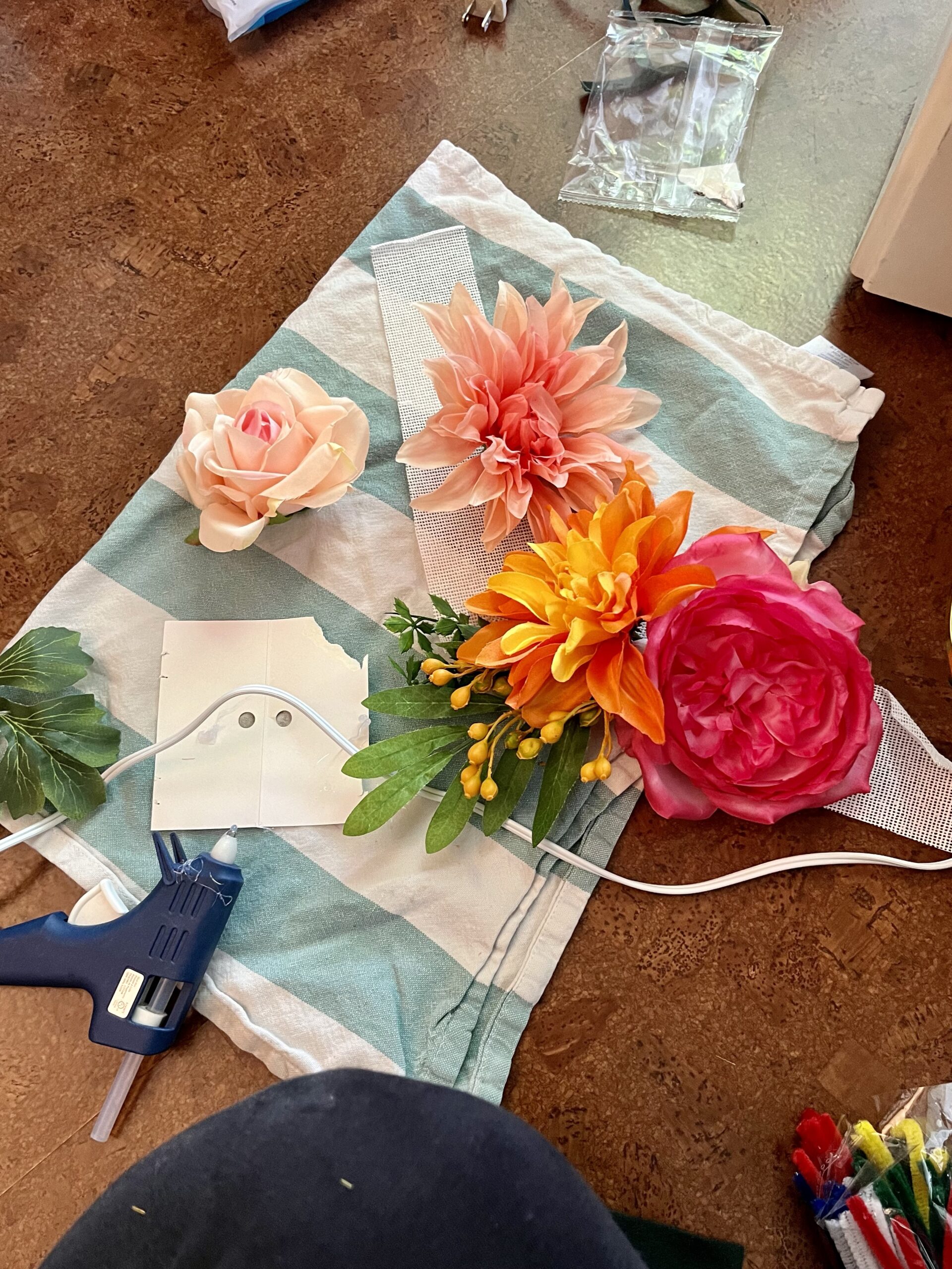 a bunch of artificial flowers and a glue gun lie on a kitchen towel