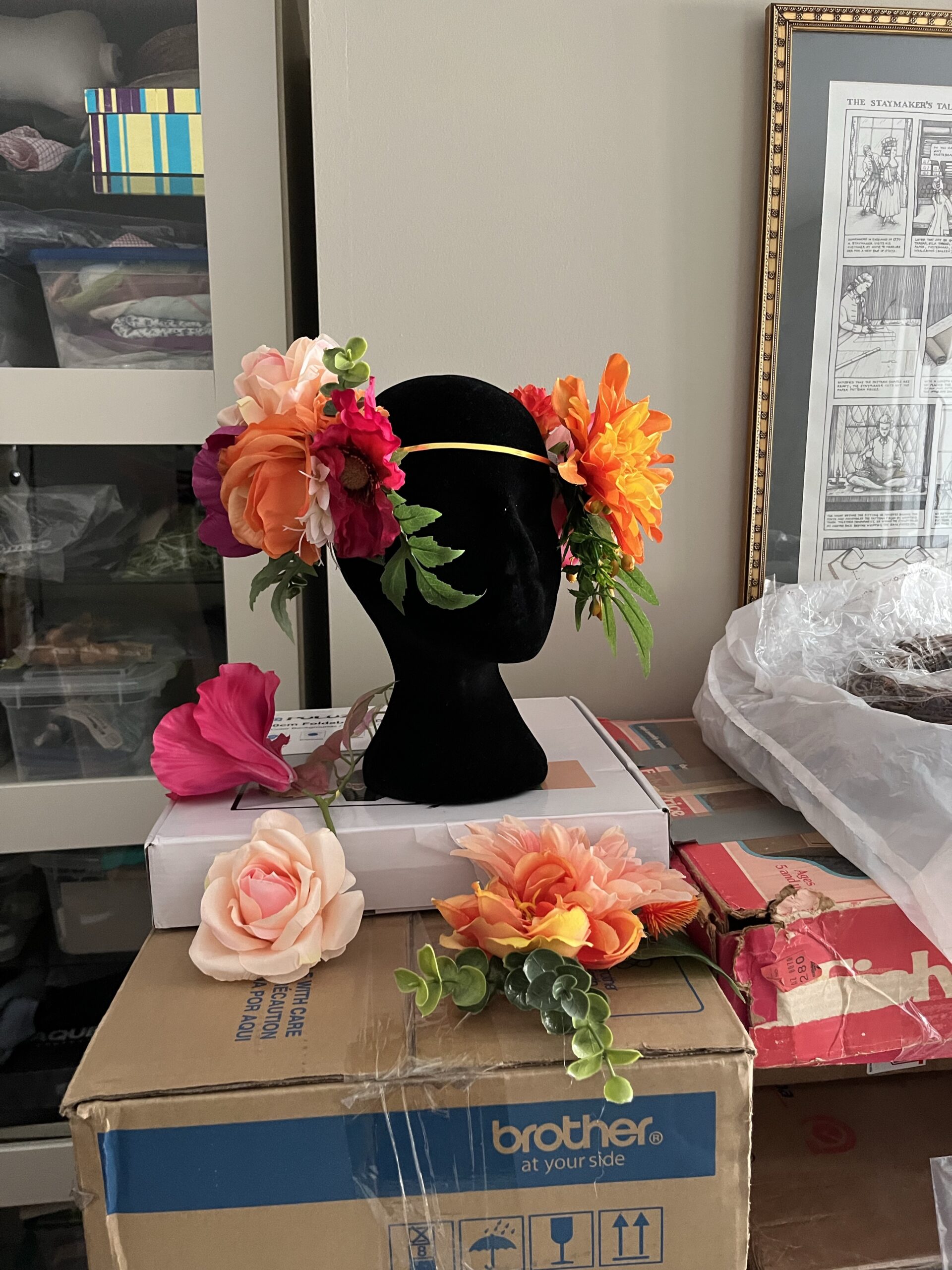 an alphonse mucha inspired mannequin head sits on top of a box. The head is surrounded by a scattering of artificial flower posies.