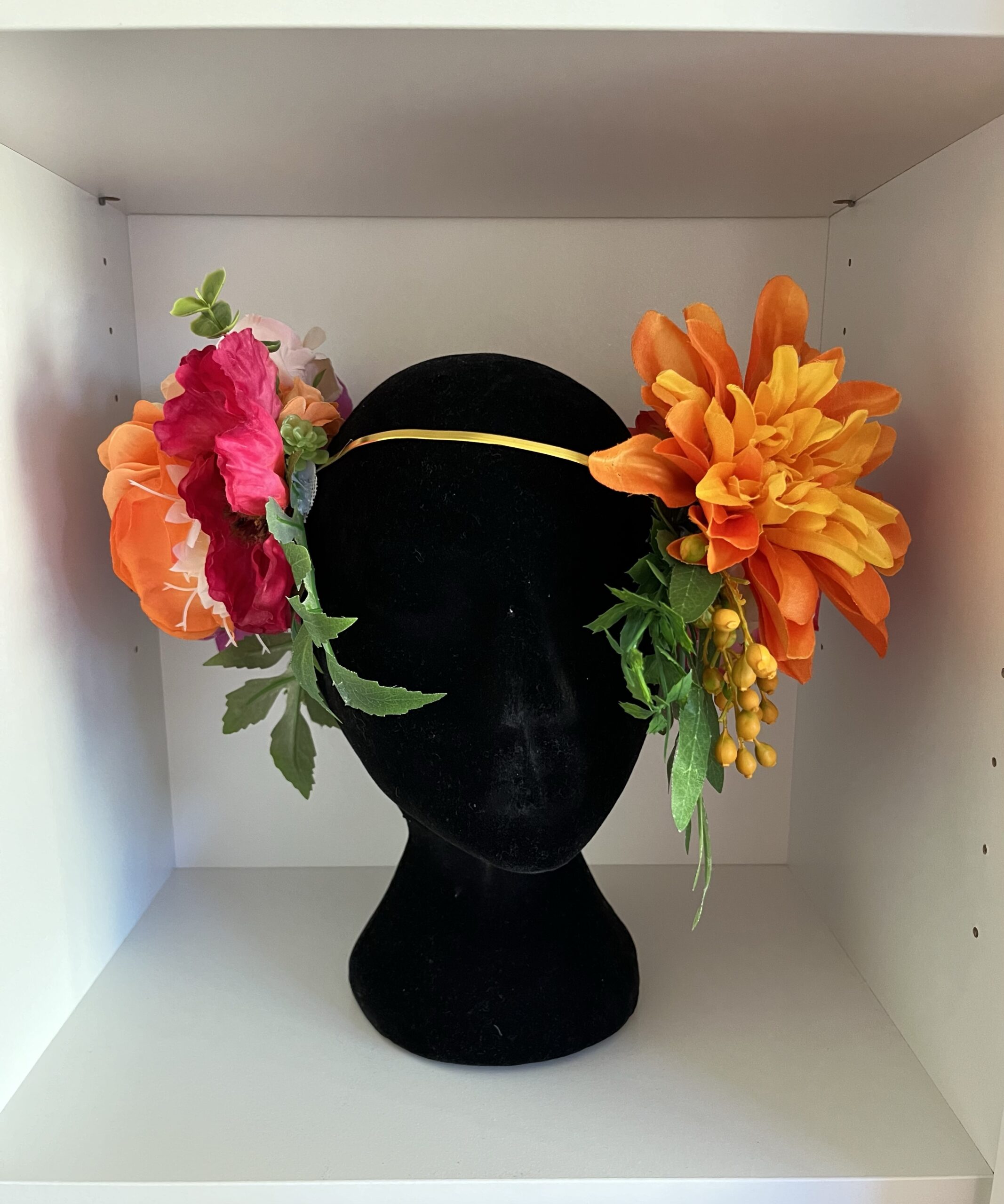 an alphone mucha inspired wreath of flowers rests on a black mannequin head inside a box