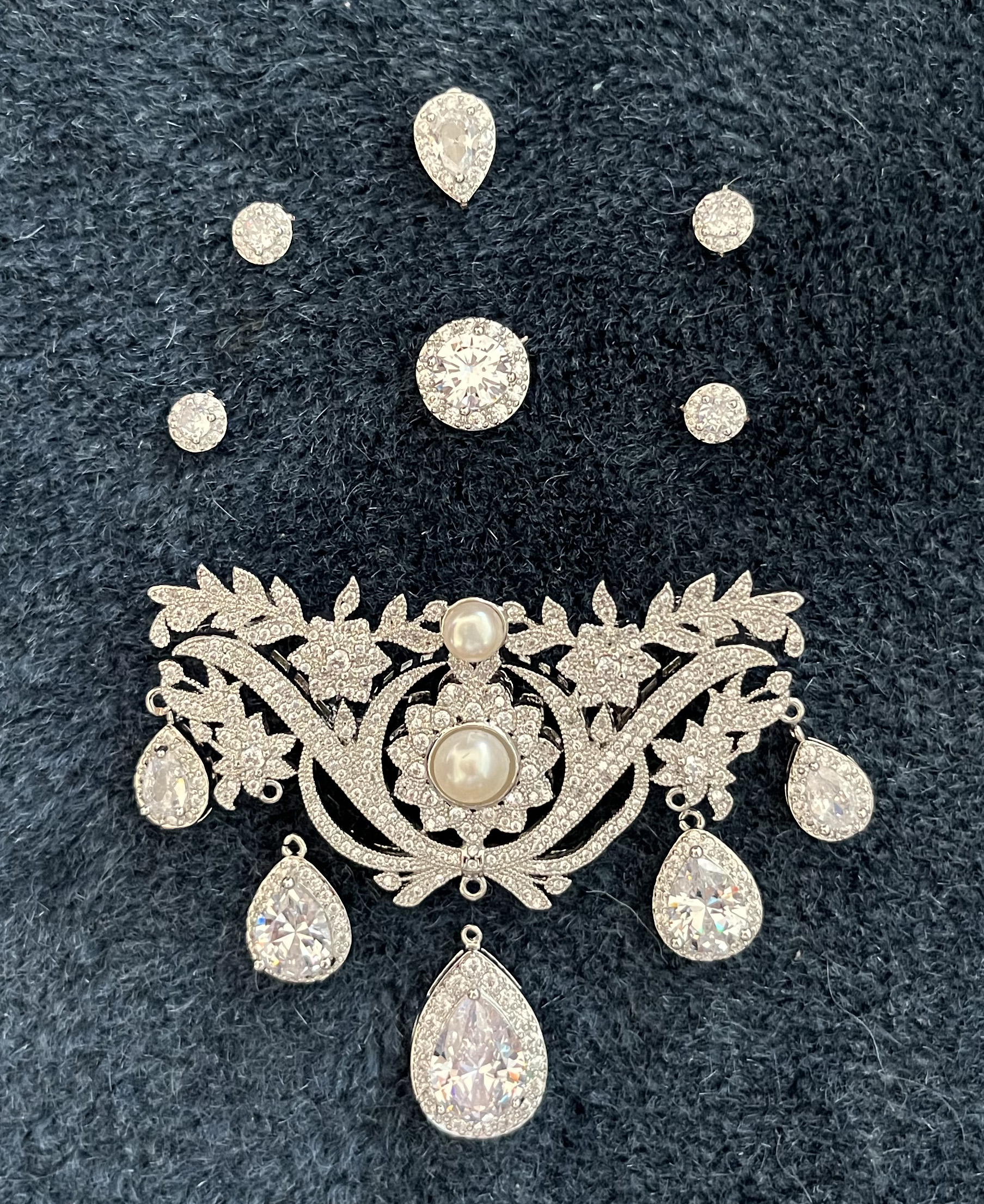 A reproduction of an 18th Century stomacher brooch lies on a blue rug surrounded by an array of sparkly rhinestone jewelry components