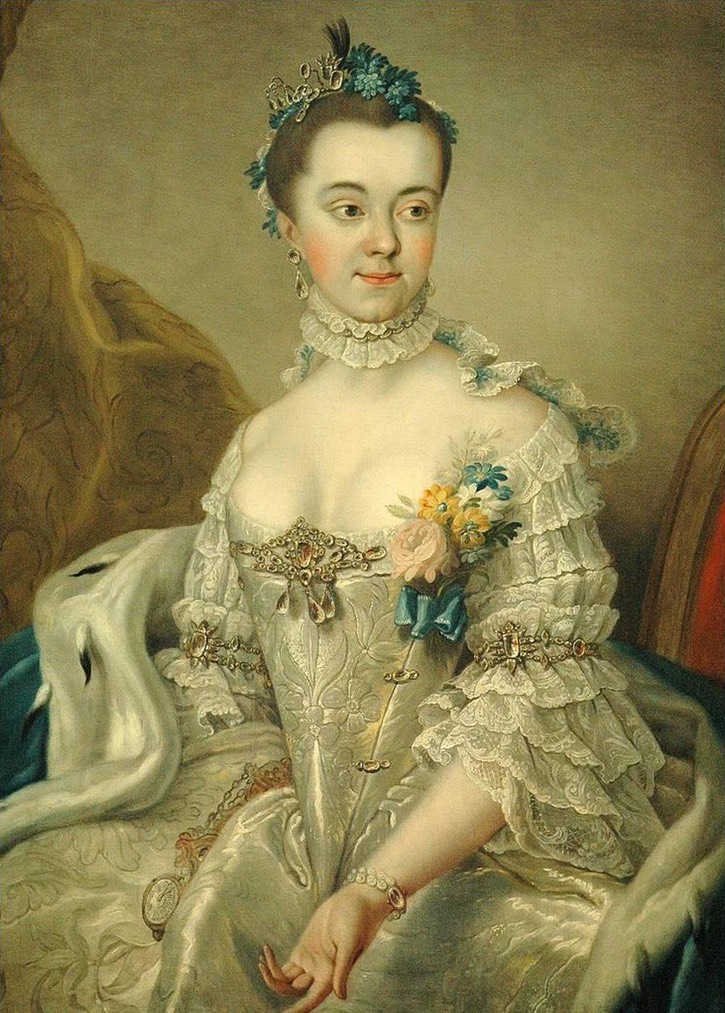 A woman in 18th century dress wears a large stomacher brooch set with pink stones