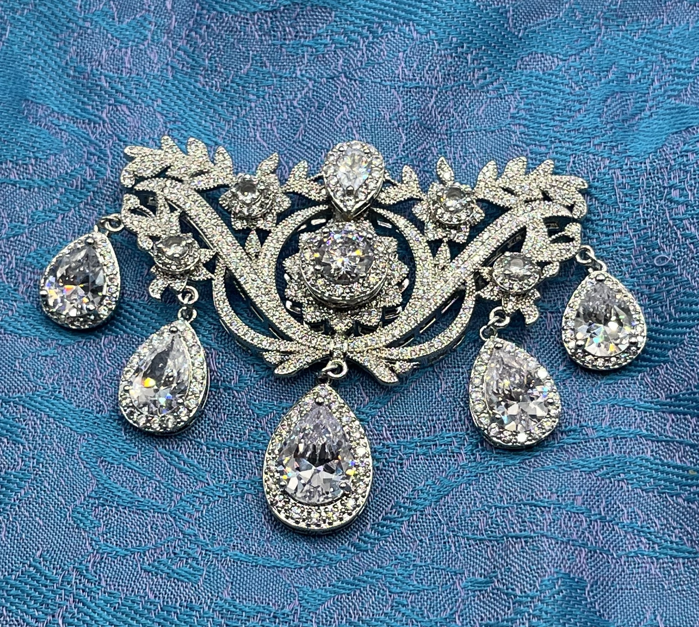 A reproduction of an 18th Century Stomacher Brooch set with rhinestones lies on a blue silk shawl