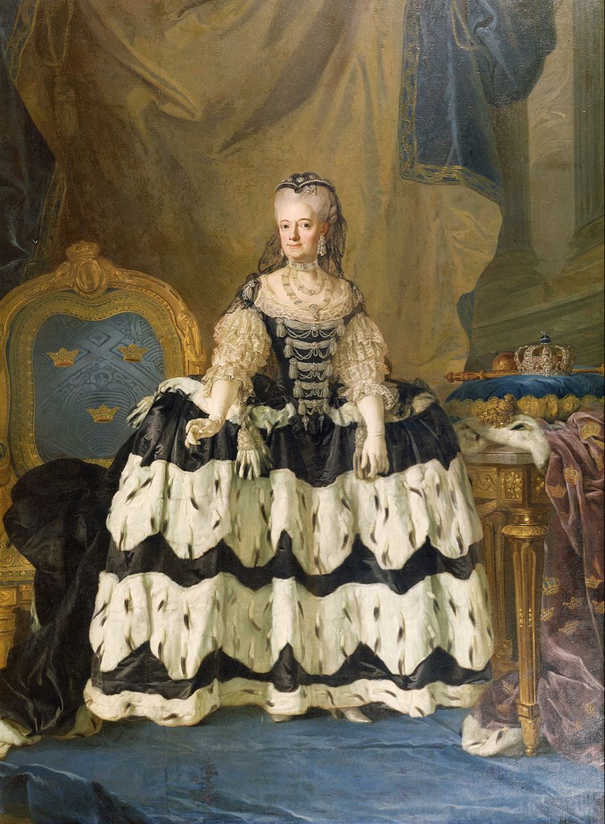 A woman stands wearing an enormous 18th century courgown of black and white with her chest covered in an enormous pearl stomacher